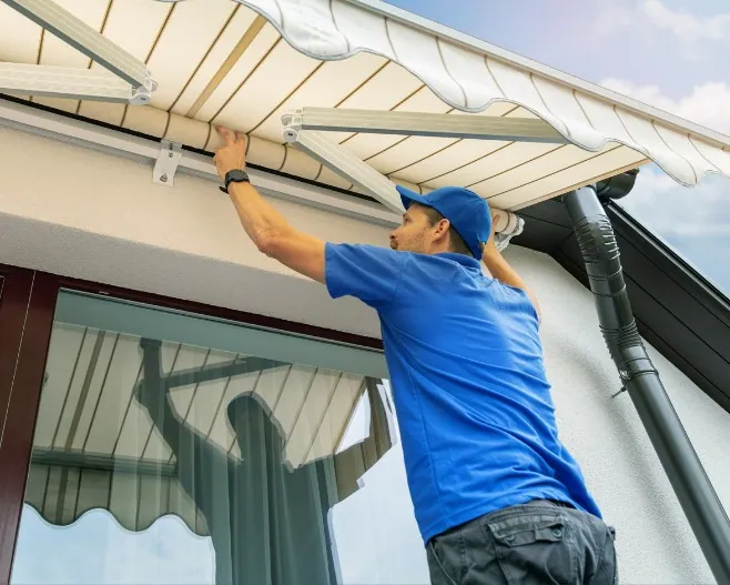 Instalador ajustando un toldo de brazo articulado Instalador ajustando el brazo articulado de un toldo sobre la puerta de una terraza