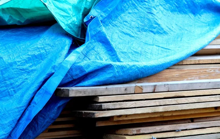 Lona de PVC azul cubriendo madera Lona azul de PVC cubriendo tablones de madera apilados