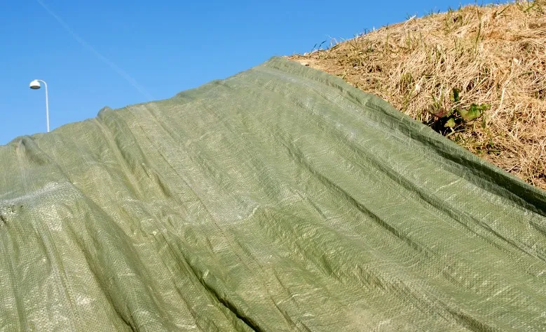 Lona verde de protección para material Lona verde de protección tensada cubriendo material apilado al aire libre