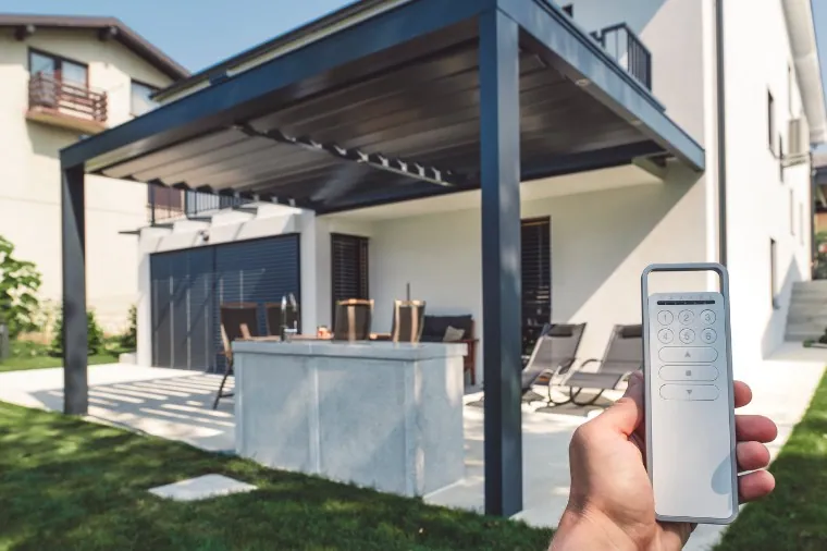 Mando de una pérgola bioclimática motorizada Mano sujetando el mando de una pérgola motorizada en un jardín