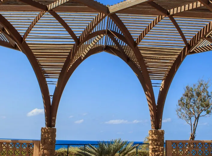 Pérgola de madera con arcos y celosía frente al mar