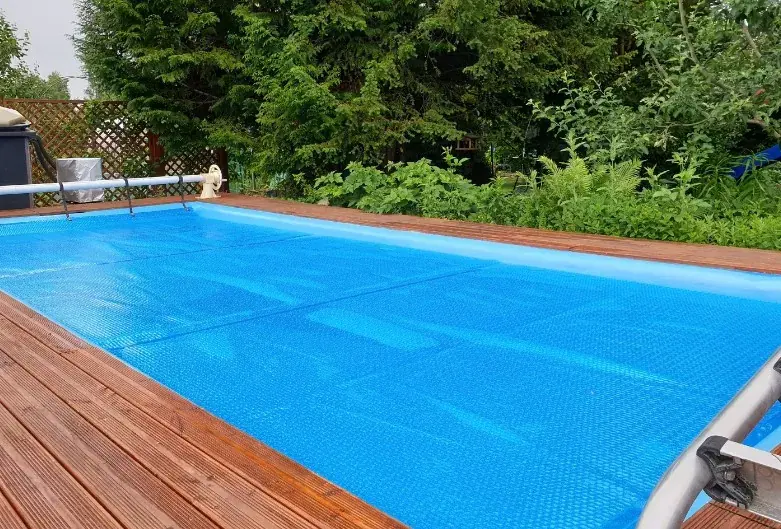 Manta térmica de burbujas en piscina Piscina cubierta con manta térmica de burbujas azul junto a tarima de madera
