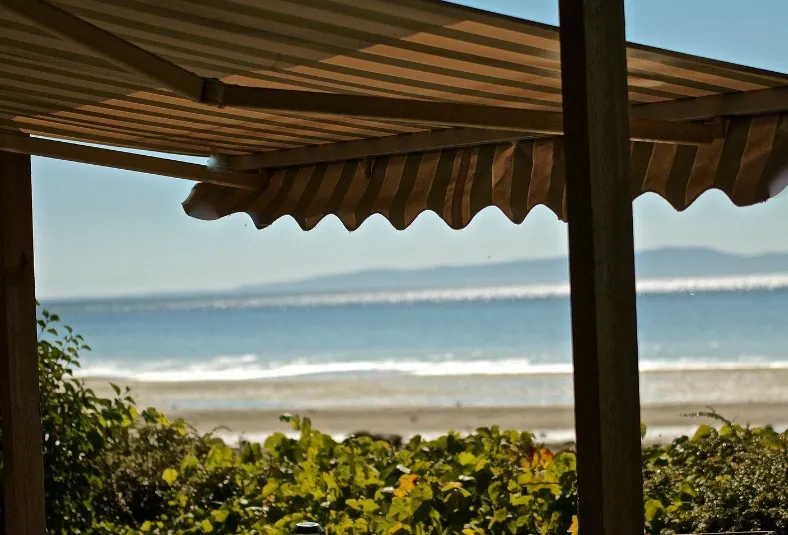 Toldo de brazos con lona beige en un porche de madera frente a la playa