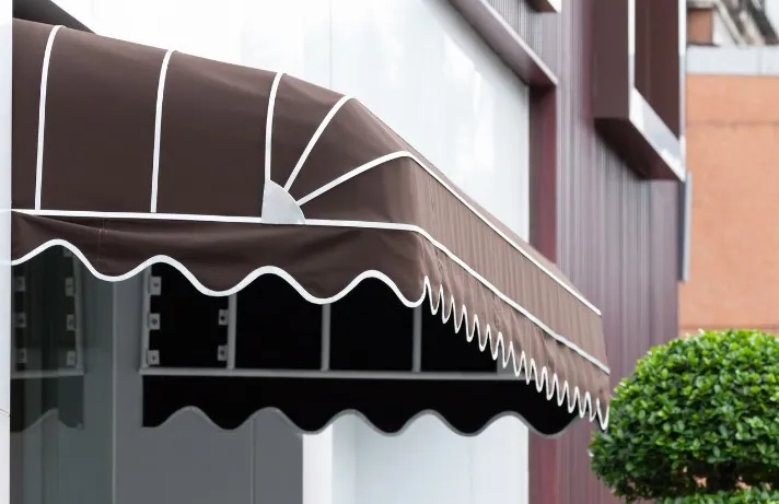 Toldo de capota marrón en entrada de comercio Toldo de capota marrón con volante blanco en la entrada de un comercio