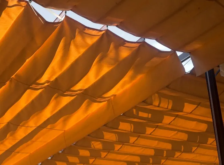 Palillería con lona naranja Lona naranja de palillería plegada en ondas bajo una pérgola