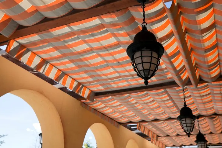 Lona de palillería a rayas naranjas bajo un porche con arcos y farolas