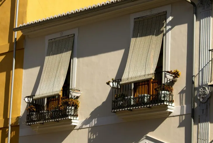 Toldos verticales en ventanas Toldos verticales de tejido microperforado bajados en las ventanas de una fachada amarilla